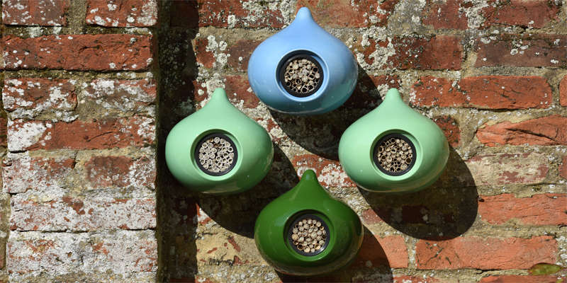 Beepalaces with nesting bees in blue, sage and ivy on a red brick wall